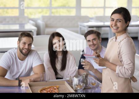 Porträt einer hübschen indischen Kellnerin, die eine Gruppe von Gästen bedient Stockfoto