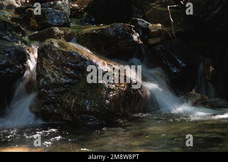 Nahaufnahme von bewegungsunscharfen Stromschnellen, die über einen Stein fließen Stockfoto