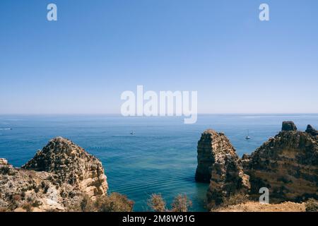 NATUR MIT DEM MEER AM HORIZONT AN EINEM SONNIGEN TAG MIT BLAUEM HIMMEL IN DEN BOOTEN DER ALGARVE IN DER GEGEND UND GROSSEN KLIPPEN Stockfoto