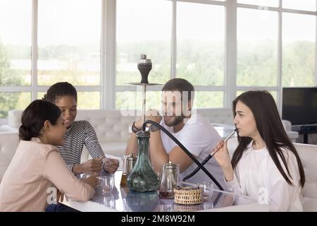 Verschiedene Mädchen und Männer, die ihre Freizeit in der Hookah Lounge genießen Stockfoto