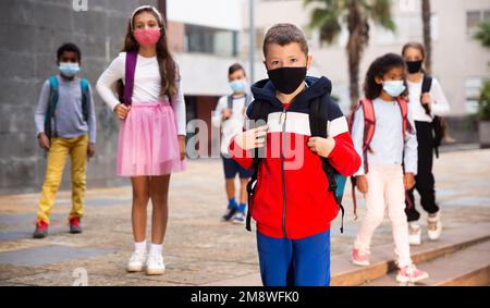 Schuljunge in medizinischer Maske in der Nähe der Schule, Kinder auf dem Hintergrund Stockfoto