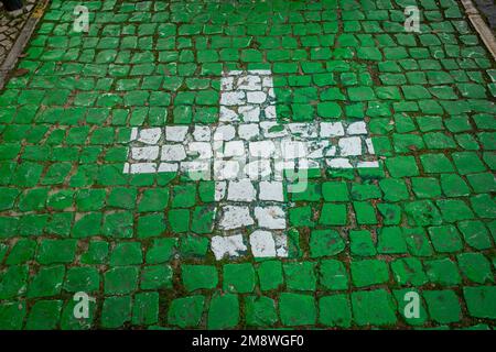 Weißes Kreuz auf grünem Fliesenhintergrund, Apothekenparkplatz in Portugal. Stockfoto