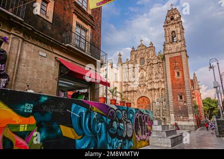 Eine mit Graffiti markierte Wand führt zur churrigueresken Fassade der Kirche Parroquia de la Santísima Trinidad im Stadtviertel Zona Centro von Mexiko-Stadt, Mexiko. Stockfoto