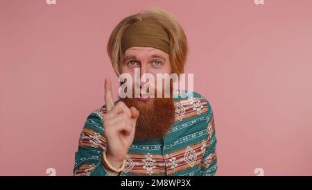 Hippie-Rothaarige mit Bart schüttelt den Finger und sagt nein, sei vorsichtig, schimpft und gibt Ratschläge, um Gefahr zu vermeiden Fehler, Missbilligung Zeichen. Hipster-Ginger-Typ mit pinkfarbenem Studiohintergrund Stockfoto