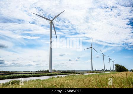 Windturbinen und Sonnenkollektoren am Ufer eines Kanals auf dem Land an einem teilweise bewölkten Sommertag Stockfoto