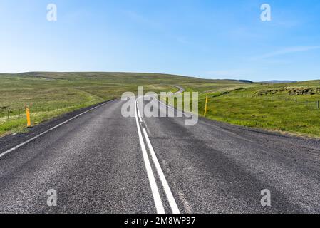 Verlassene gewundene Straße durch grasbedeckte Hügel in Island an einem klaren Sommertag Stockfoto