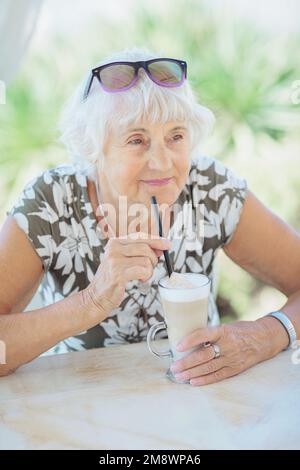 Attraktive Seniorin, die in einem Sommerkaffee im Freien sitzt Stockfoto