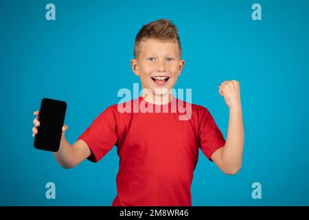 Aufgeregter junger Junge, der sein Smartphone mit einem leeren schwarzen Bildschirm vor der Kamera vorführt Stockfoto