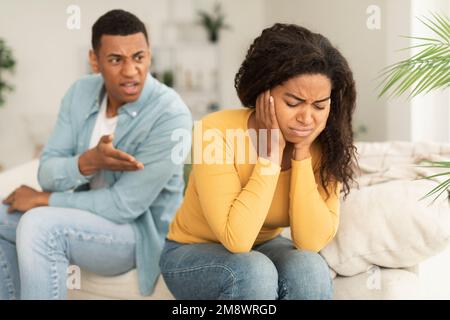 Traurige, weinende junge afroamerikanische Frau ignoriert wütenden, aggressiven schreienden Kerl, der auf dem Sofa sitzt Stockfoto