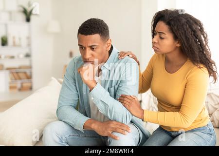 Entschuldige dich zu Hause. Traurige junge afroamerikanische Frau beruhigt den Kerl, Unterstützung und Fürsorge, auf dem Sofa sitzen Stockfoto