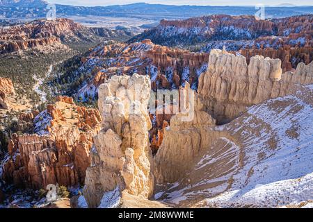 Der Bryce Canyon ist mit frisch gefallenem Schnee und fernen Bergen und leuchtend farbigen orangefarbenen Klippen geschmückt. Stockfoto