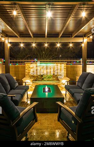 Ein Garten im Resortstil bei Nacht mit Wasserfall, Pergola und einer Feuerstelle bei Nacht. Stockfoto