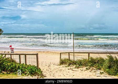 Weg zum Strand mit Drahtzaun und Vegetation auf jeder Seite, stürmische Wellen und ein Schild mit der Aufschrift Gefahr Schwimmen verboten Stockfoto