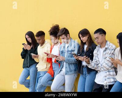 Eine Gruppe unterschiedlicher Schüler chatten und sehen sich digitale Inhalte auf Mobiltelefonen an. Der Begriff der Technologieabhängigkeit und soziale Netzwerke Stockfoto