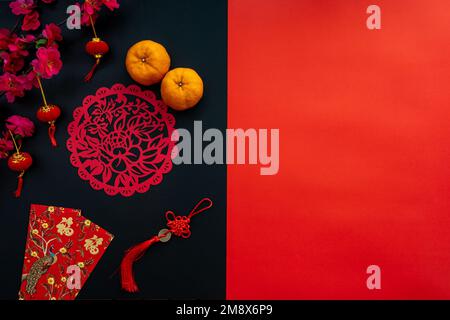 Dekoration im chinesischen Neujahrsmond auf rotem und schwarzem Hintergrund. Flaches Lagekonzept mit Mandarine, rotem Umschlag, Pflaume und festlicher Dekoration. Stockfoto