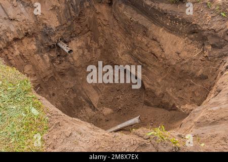 Große tiefe Grube im Boden nach dem Ausheben eines Abwasserrohrs eines Hydraulikbaggers in einem Industriegebiet. Stockfoto