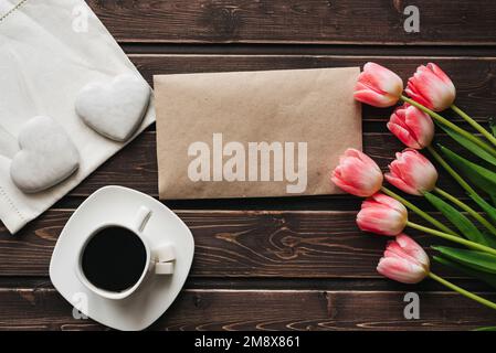 Strauß rosa Tulpen mit einer Tasse Kaffee und weißem Lebkuchen in Herzform für das morgendliche Frühstück auf einem Holztisch. Frühlingsgrüße Stockfoto