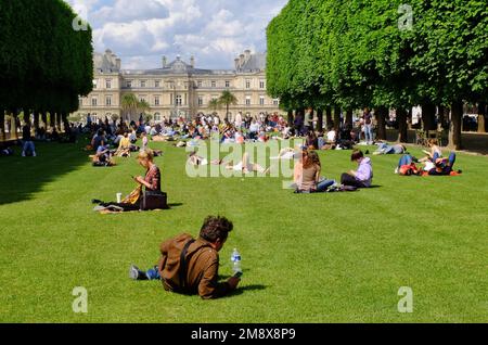 Paris: Menschen, die sich in der Sonne auf dem Gras des Palais und des Jardin du Luxembourg in Paris, Frankreich, entspannen Stockfoto