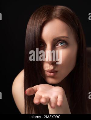 Eine Frau, die Lippen bläst, ihrem Freund Luftküsse über die Handfläche schickt, flirtet - nur für dich. 40-jährige weiße Frau mit langen Haaren, die Liebe zeigt Stockfoto