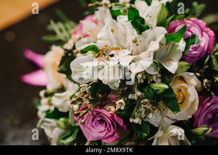Zwei goldene Eheringe mit Diamanten liegen auf einem Blumenstrauß Stockfoto