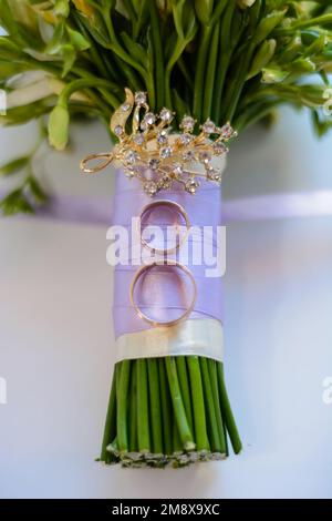 Ein Paar goldene Ringe liegen auf dem Blumenstrauß der Braut Stockfoto