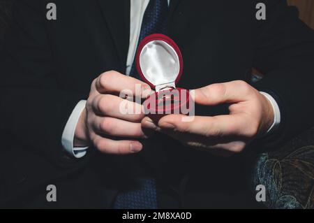 Zwei goldene Eheringe liegen in einer roten Schachtel auf der männlichen Hand des Bräutigams Stockfoto