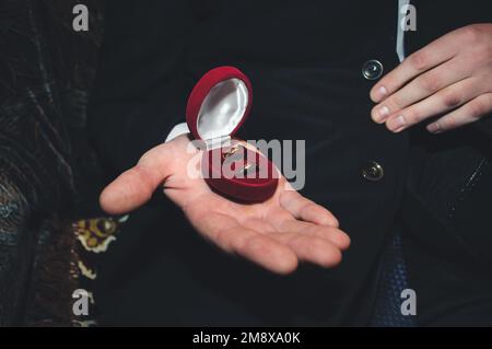 Zwei goldene Eheringe liegen in einer roten Schachtel auf der männlichen Hand des Bräutigams Stockfoto