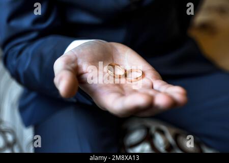 Zwei goldene Eheringe in den Händen des Mannes des Bräutigams Stockfoto