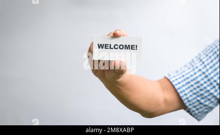 Mann mit weißer Visitenkarte mit Text, Willkommen! Auf weißem Hintergrund. Stockfoto