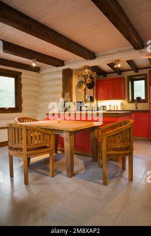 Hölzerner Frühstückstisch mit runden Lehnstühlen und Blick auf die Küche mit roten Holzschränken im 1. Stock im Blockhaus im skandinavischen Stil. Stockfoto