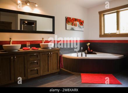 Hauptbadezimmer mit braunem Holzschrank mit seinen und ihren weißen Waschbecken und ummantelter Badewanne im Obergeschoss im Blockhaus im skandinavischen Stil. Stockfoto