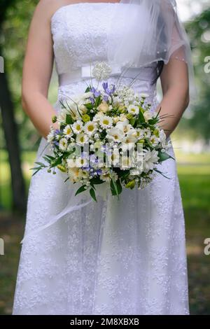 Ein Blumenstrauß in den Händen der Braut in einem weißen Kleid Stockfoto