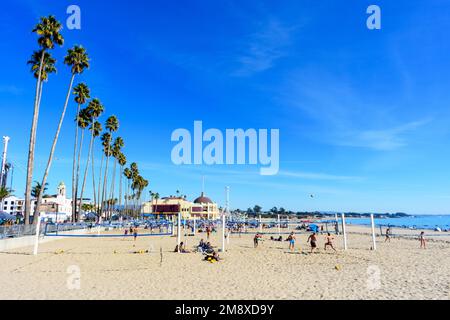 Boardwalk Beach mit Palmen in Reihe, Volleyballplätzen und Menschen. Der Santa Cruz Beach Boardwalk ist im Hintergrund - Santa Cruz, Kalifornien, USA Stockfoto