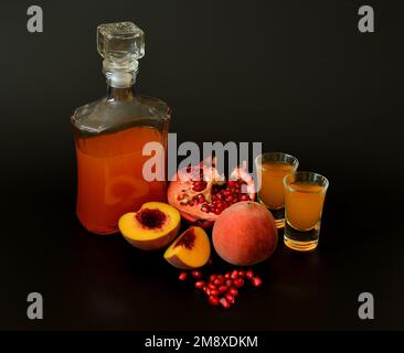 Fruchtlikör in einer Flasche und zwei Gläser auf schwarzem Hintergrund, neben reifem Pfirsich und Granatapfelfrüchten. Nahaufnahme. Stockfoto