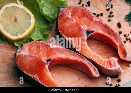 Stücke von rotem Fischfilet. Frischer roher Lachs auf einem Holzbrett mit Gewürzen und Zitrone Stockfoto