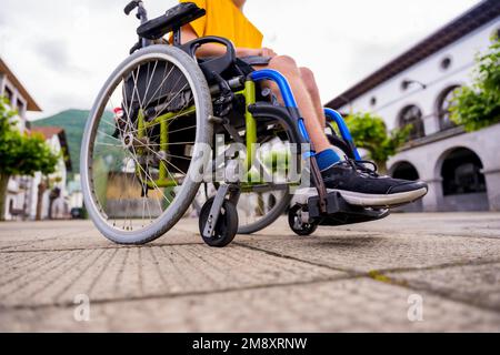 Detail einer behinderten Person in einem Rollstuhl, die durch den Stadtplatz geht Stockfoto