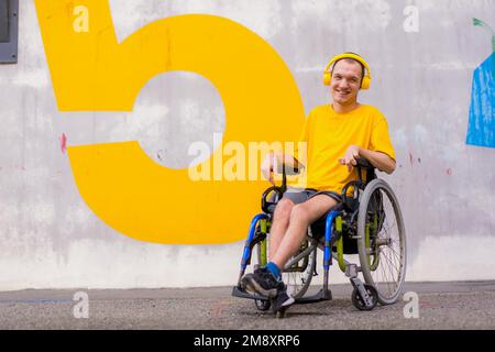 Porträt einer behinderten Person in gelber Kleidung im Rollstuhl, die lächelt und Musik hört Stockfoto