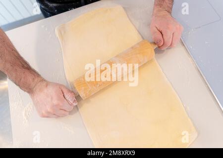 Mann backt hausgemachte Croissants, bereitet das Blätterteig zu und fügt Mehlkonfekt zu Hause hinzu Stockfoto