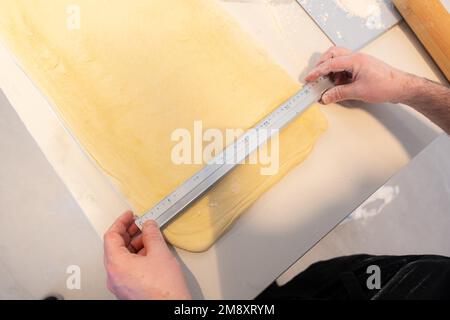 Der Konditor backt selbstgemachte Croissants, misst Blätterteig für Schnitte, arbeitet zu Hause Stockfoto