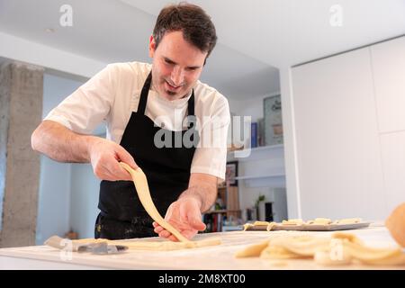 Ein Mann, der Croissants backt, die dreieckigen Schnitte vom Blätterteig aufnimmt, arbeitet zu Hause Stockfoto