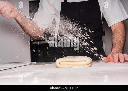 Der Konditor backt selbstgemachte Croissants, bereitet den Blätterteig zu und fügt Mehl hinzu, arbeitet zu Hause Stockfoto