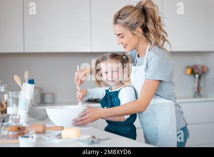 Porträt eines kleinen Mädchens, das mit ihrer Mutter backt. Glückliche Mutter hilft ihrer Tochter beim Backen. Eltern backen mit ihrem Kind in der Küche. Mutter hilft Stockfoto