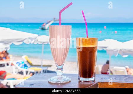 Gläser mit Milchshake und Frappe auf einem Tisch mit Blick auf den Strand. Rhodos, Griechenland Stockfoto