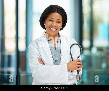 Bereit für die Untersuchung. Eine junge Ärztin, die in einem Krankenhaus mit gekreuzten Armen stand. Stockfoto