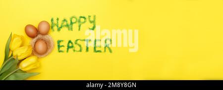 Inschrift Happy easter aus Gras mit Haseneiern, Blumen Tulpen und Nest auf gelbem Hintergrund. Platz für Text kopieren. Banner Stockfoto