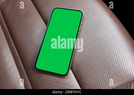 Smartphone im Auto für Navigation oder GPS. Mobiltelefon mit isoliertem grünen Bildschirm mit Chromschlüssel auf braunem perforiertem Ledersitz. Speicherplatz kopieren. Leer Stockfoto