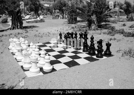 IOS, Griechenland - 6. Juni 2021 : Blick auf ein lebensgroßes riesiges Schachbrett am Strand in iOS Greece in Schwarz und Weiß Stockfoto