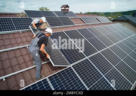 Männer Techniker Montage Photovoltaik-Solarmodule auf Dach des Hauses. Ingenieure in Helm Installation Solarpanel-System im Freien. Konzept der alternativen und erneuerbaren Energien. Luftaufnahme. Stockfoto