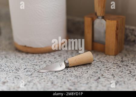 Nahaufnahme auf der Arbeitsfläche aus Marmor ist ein kleines Küchenmesser mit scharfer Edelstahlklinge und Holzgriff. Hinter, auf unscharfem Hintergrund, Papierrolle Stockfoto