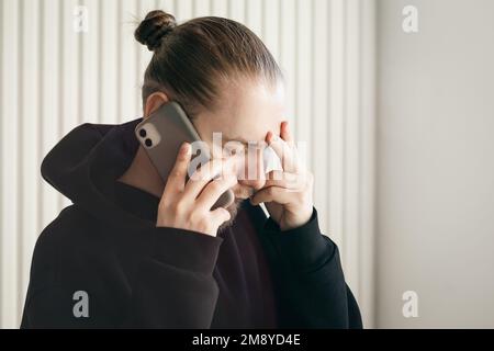 Ein junger Mann, der mit dem Smartphone spricht und seinen Kopf hält, das Konzept des Problems. Stockfoto